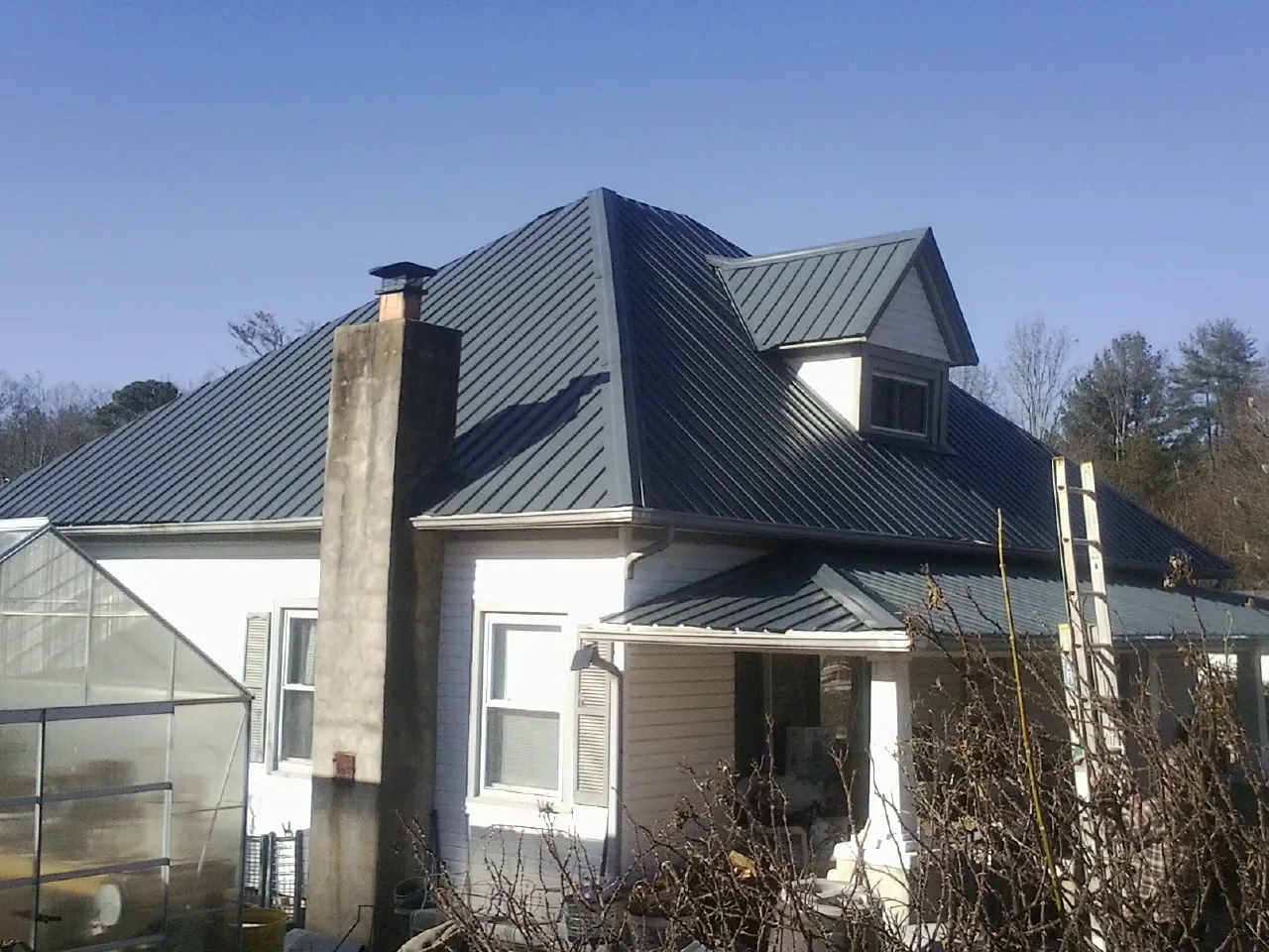 Dark blue standing seam metal roof on a white farmhouse with dormer — Slate & Tile Roof Repair by Roofing Brothers in East Baldwin