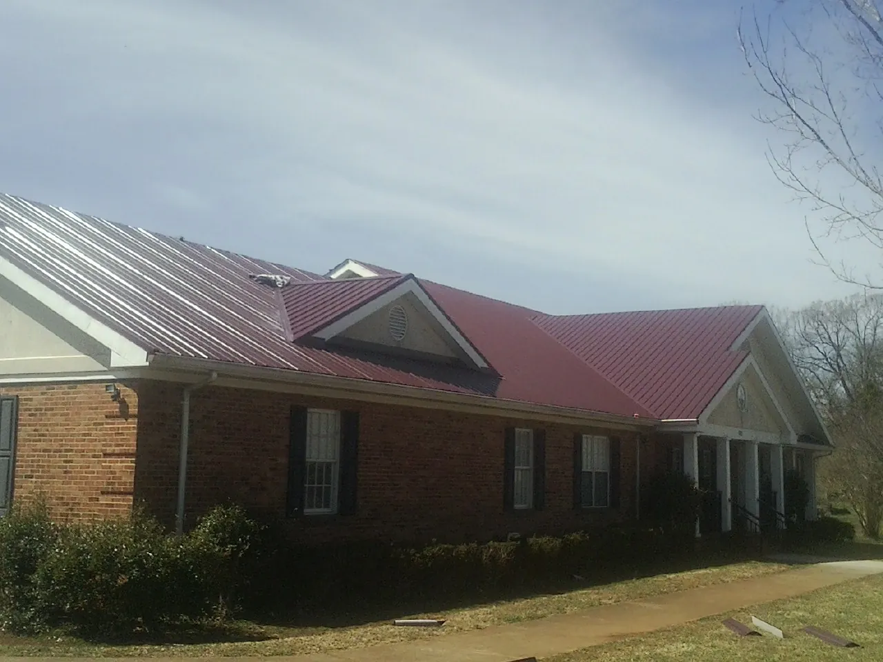 Red metal roof with gabled entries on a long brick building, from a Hail Damage Roof Repair job in East Baldwin