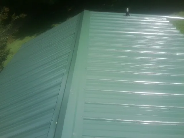 New green metal panels meeting at the ridge of a roof — Flat Roof Repair work by our crew in East Baldwin