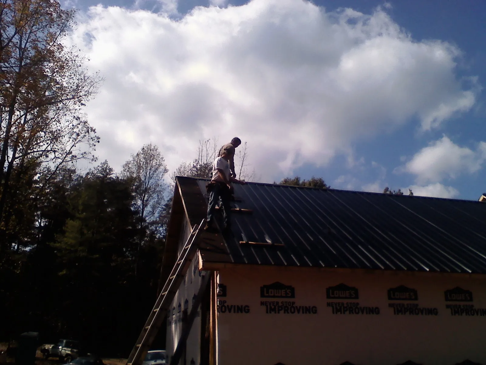 Roofer fastening dark metal panels high against a cloudy sky, from a Roof Inspection job in East Baldwin