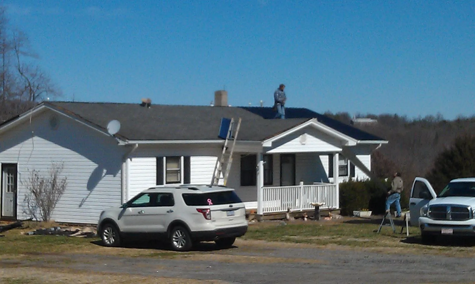 Roofers stripping shingles from a white ranch house roof in East Baldwin