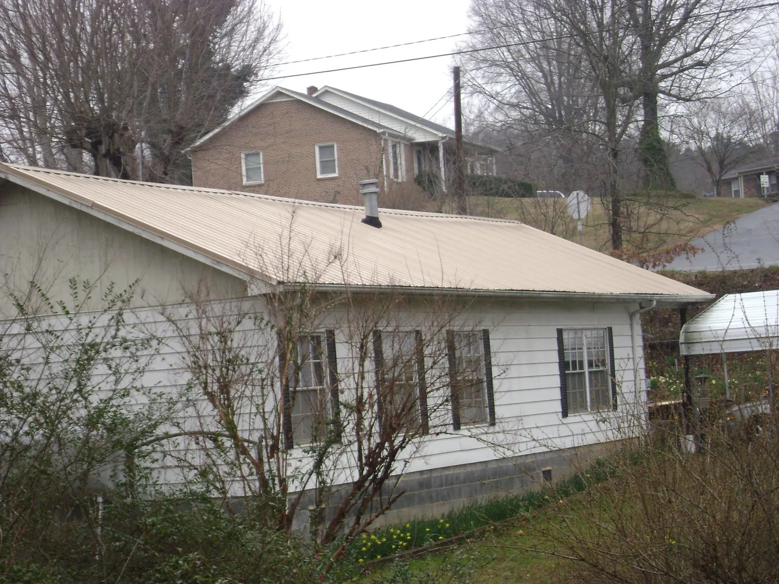 Tan metal roof on a white sided house set into a hillside — Commercial Roofing by Roofing Brothers in East Baldwin