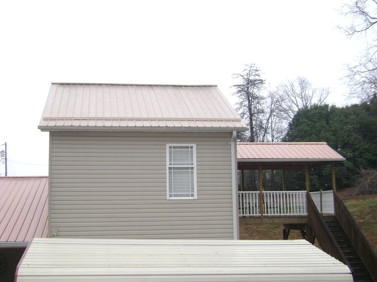 Tan metal roofs on a two story addition and attached porch, from a Roof Replacement job in East Baldwin